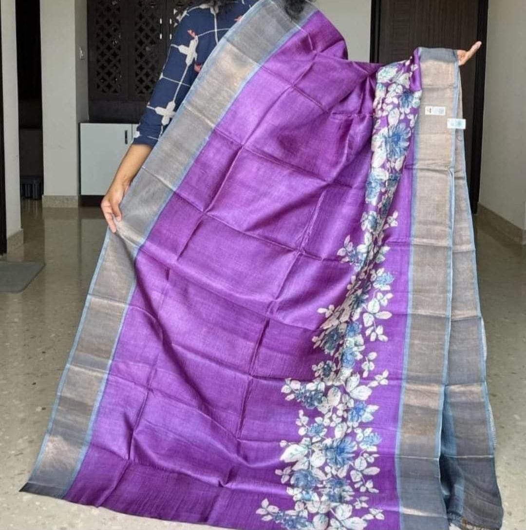 A woman holding a Handloom Bhagalpuri Tussar Saree with a panel design featuring gold borders and a floral pattern in purple and blue colors.