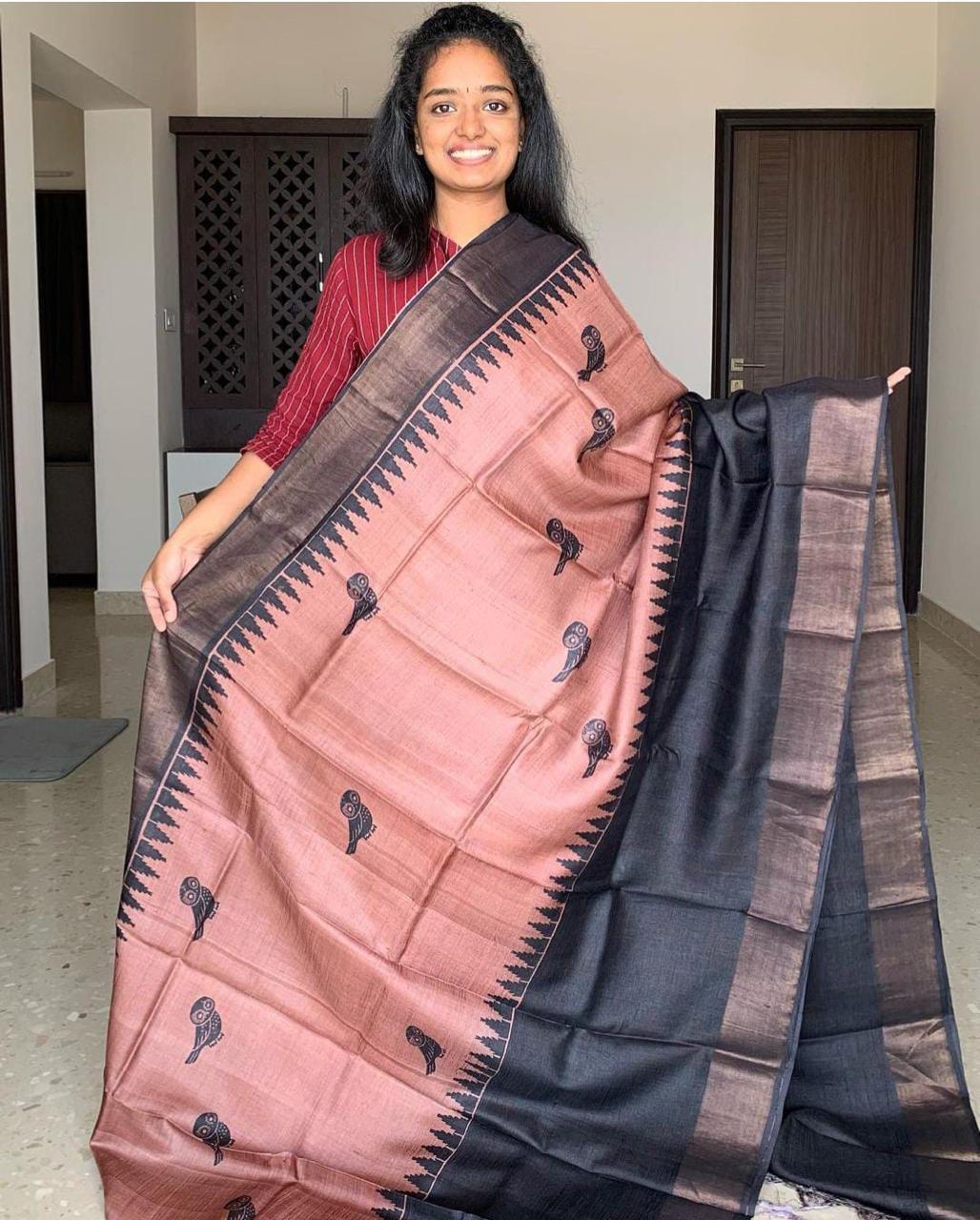 A woman holding a Handloom Bhagalpuri Tussar Saree with gold borders and a panel design, featuring a mix of dark and light colors.