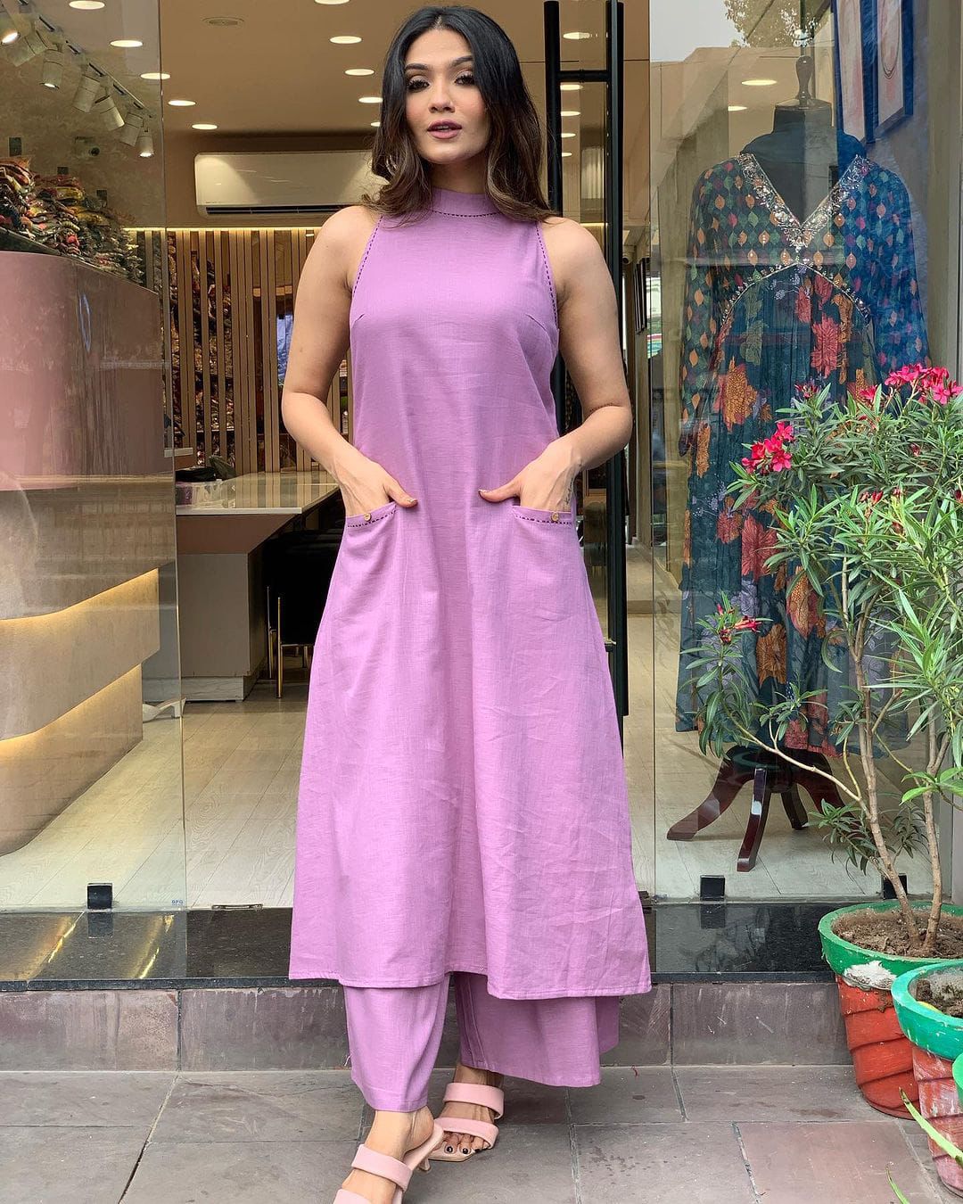 A woman standing in a store wearing a pink sleeveless cotton kurti with attached sleeves and a matching palazzo pant.