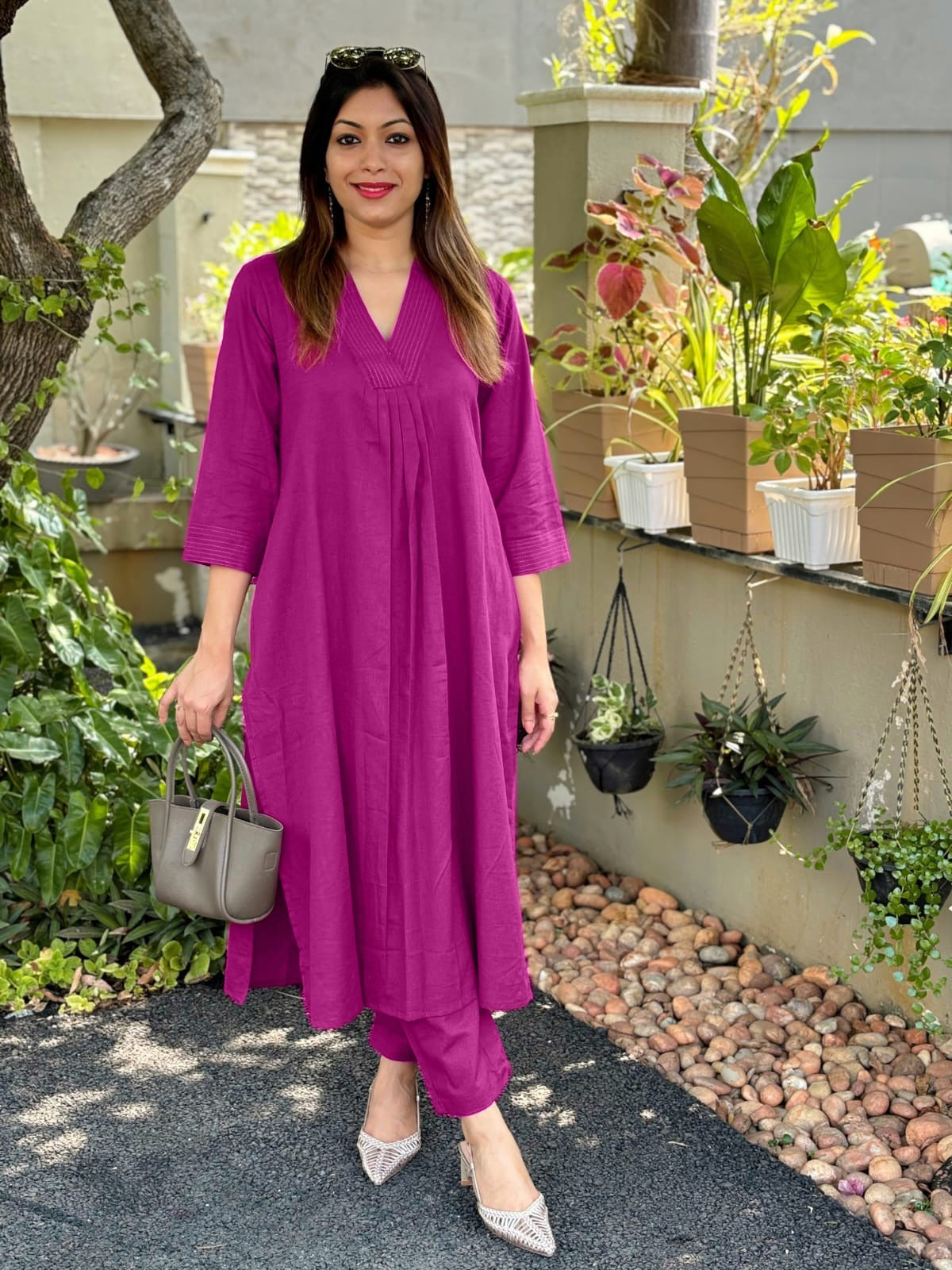 A woman wearing a pink cotton co-ord set with V-neckline and delicate detailing on the neck and sleeves, standing in a garden setting.