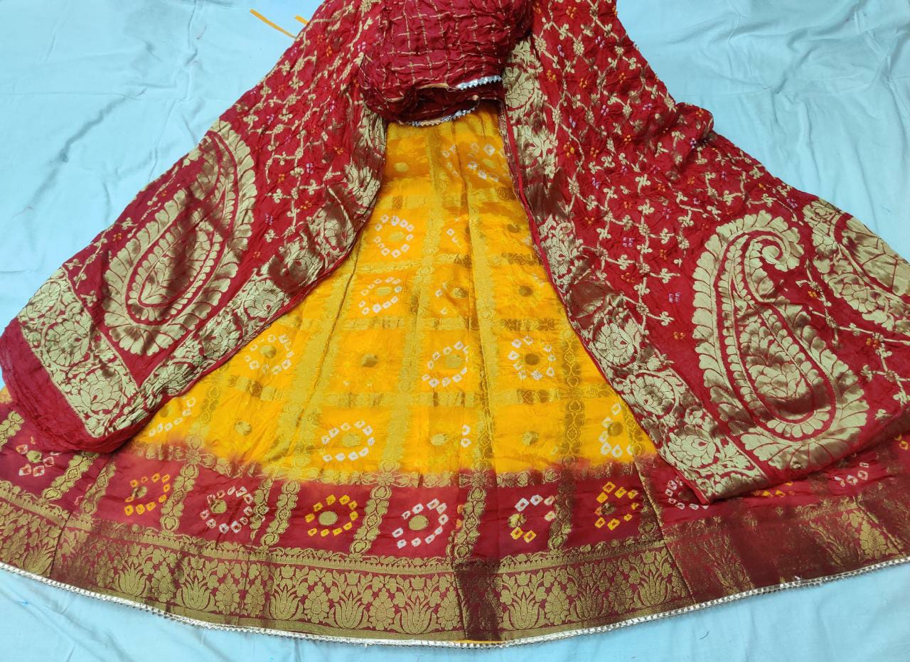 A Banarasi Gharchola silk lehenga set with a bandhani design, zari blouse, and dupatta, primarily in red and yellow colors with golden and silver embellishments.