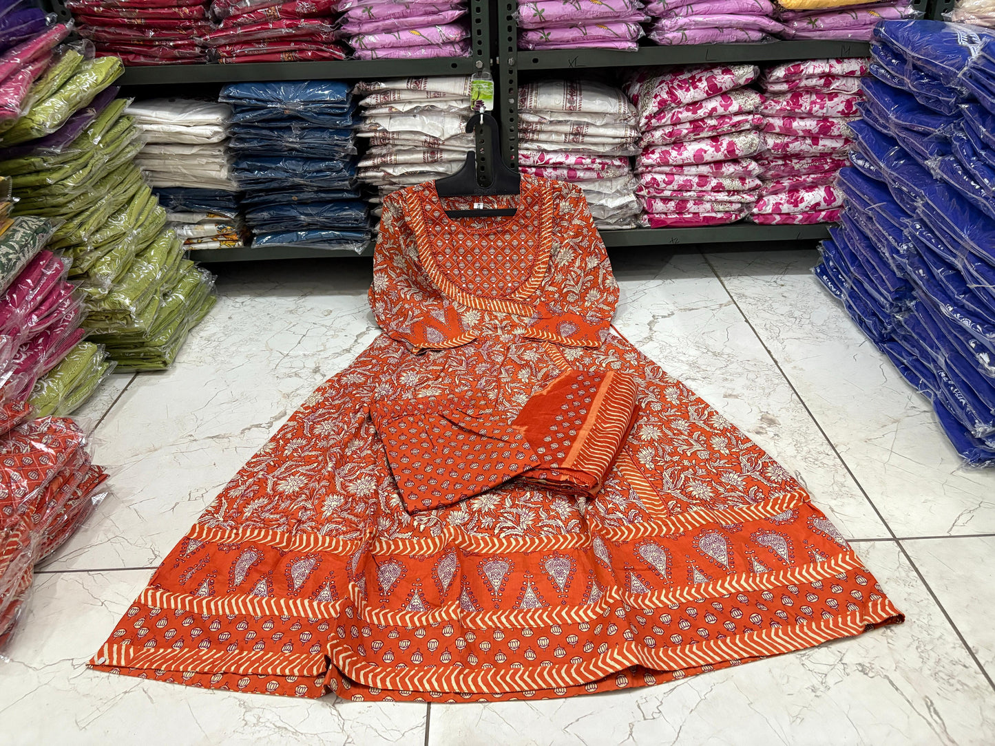 Orange patterned fabric on a stand with shelves of folded fabric in the background