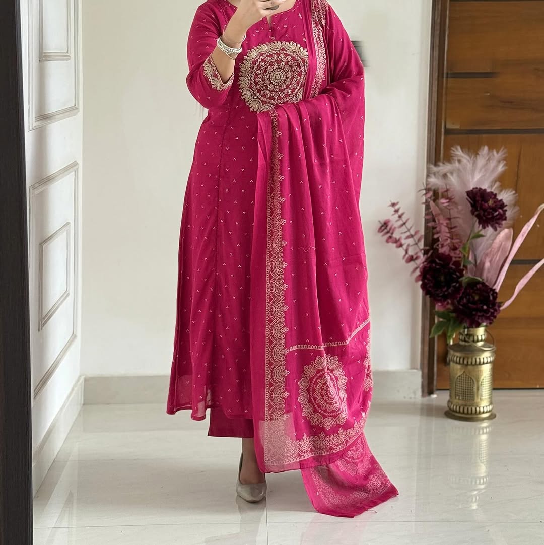 Person wearing a pink traditional outfit with intricate patterns, standing indoors.