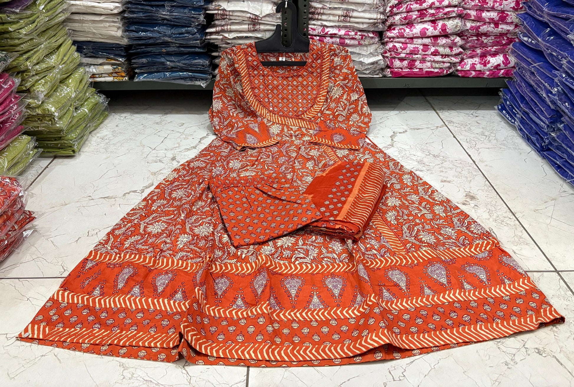 Orange and white patterned fabric on a tiled floor with stacks of folded fabric in the background.