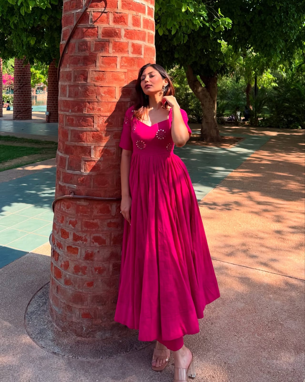 Woman in a pink dress standing next to a brick column outdoors