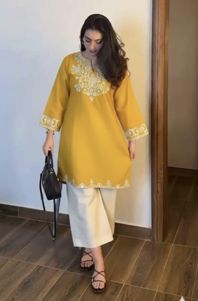 Woman wearing a yellow embroidered kurta with white pants, standing indoors.