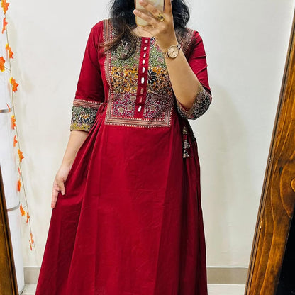 Person wearing a red traditional outfit with intricate patterns, standing in front of a mirror.