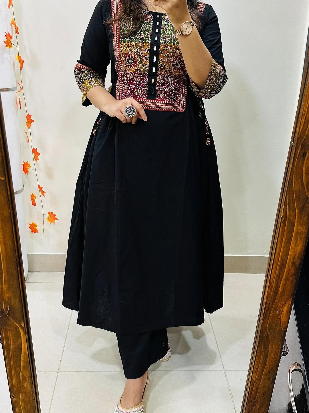 Person wearing a black outfit with colorful embroidery in front of a mirror.