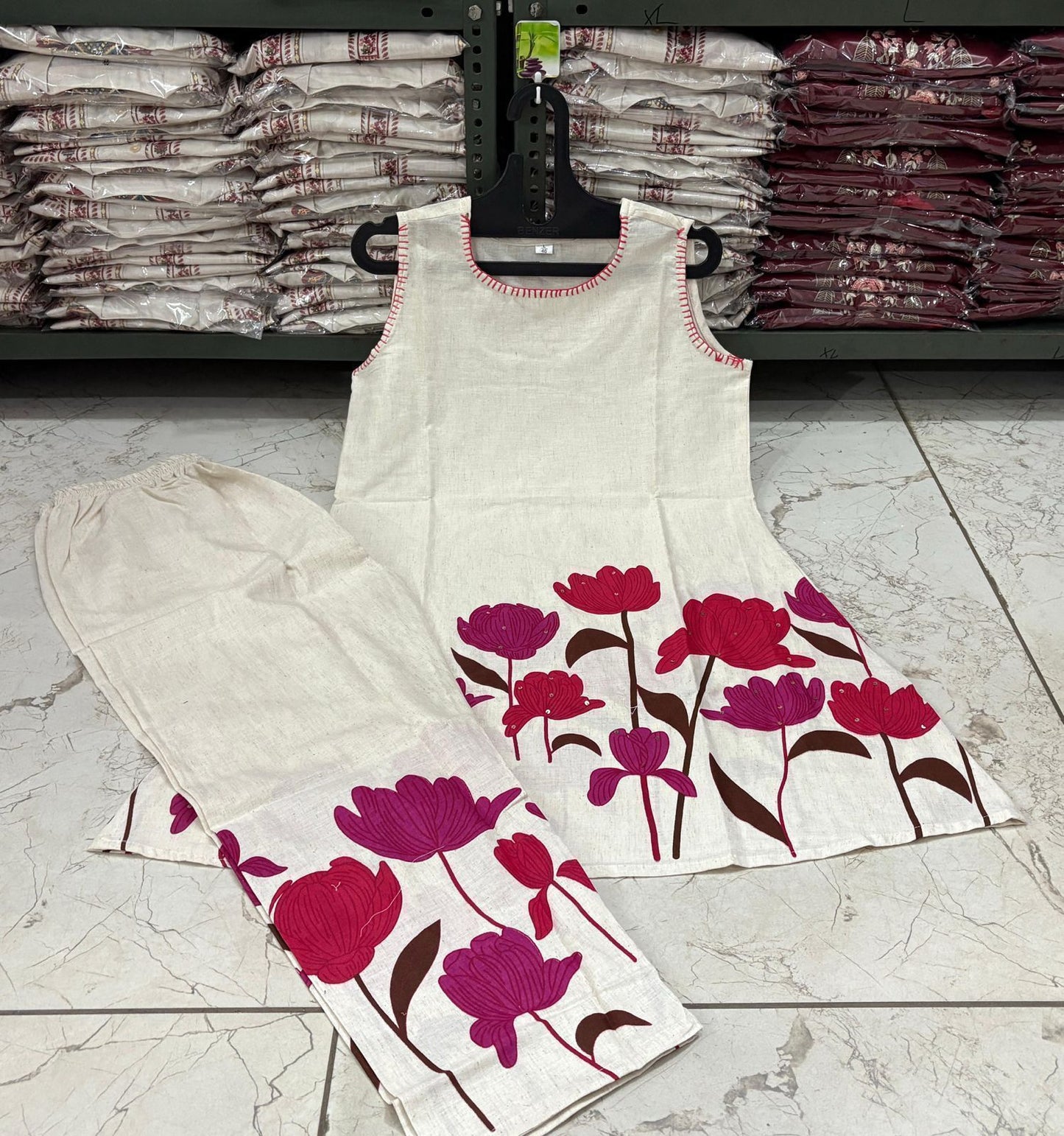 Floral-patterned fabric on a hanger with stacks of fabric in the background.