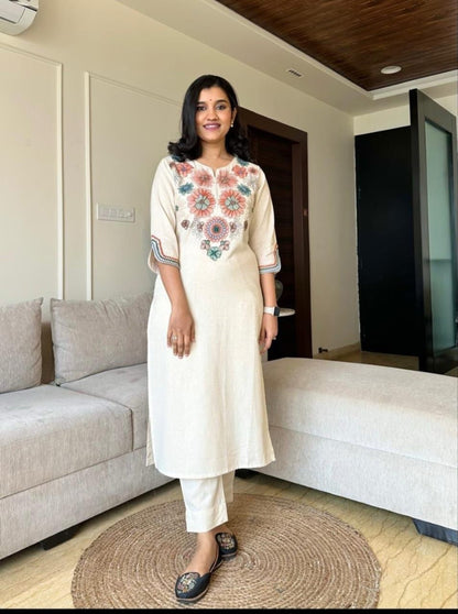 Woman in a white kurta with floral embroidery standing in a living room.