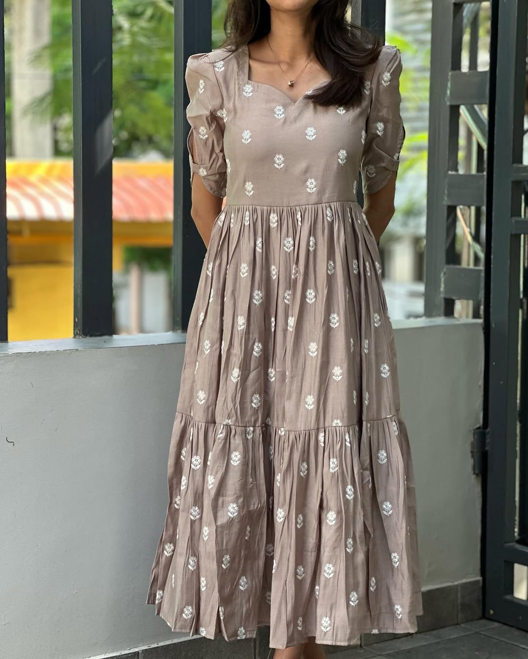 Woman wearing a beige floral dress standing in front of a glass door.
