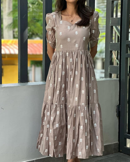 Woman wearing a beige floral dress standing in front of a glass door.