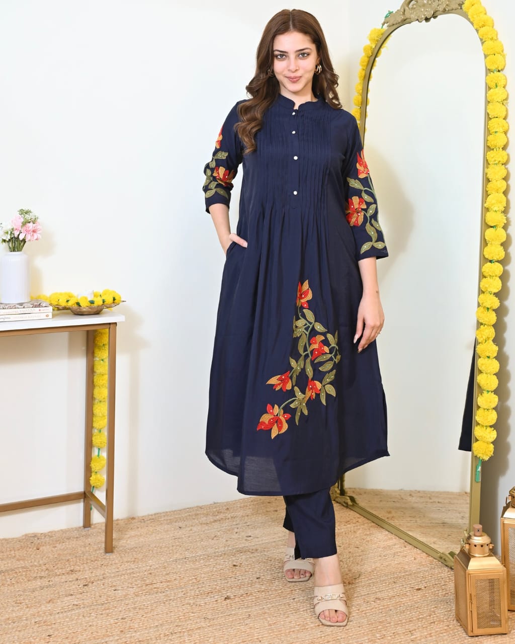Woman wearing a navy blue kurta with floral embroidery in a decorated room.