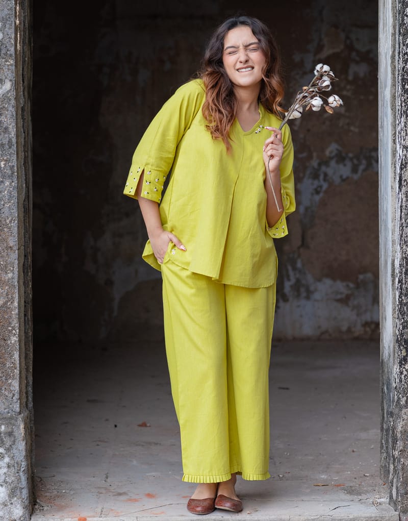 Woman in a bright yellow outfit holding a dried flower in a rustic setting