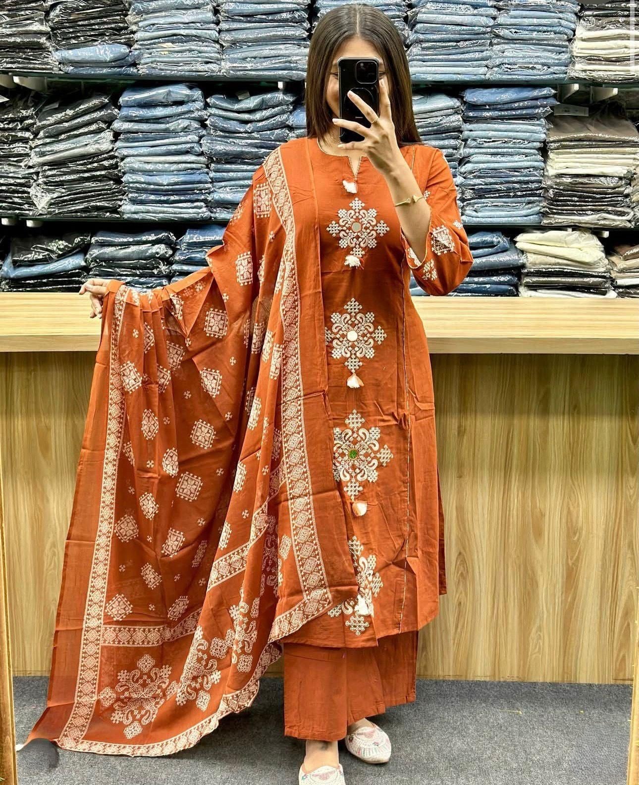 A woman wearing an orange embroidered outfit in a fabric store.