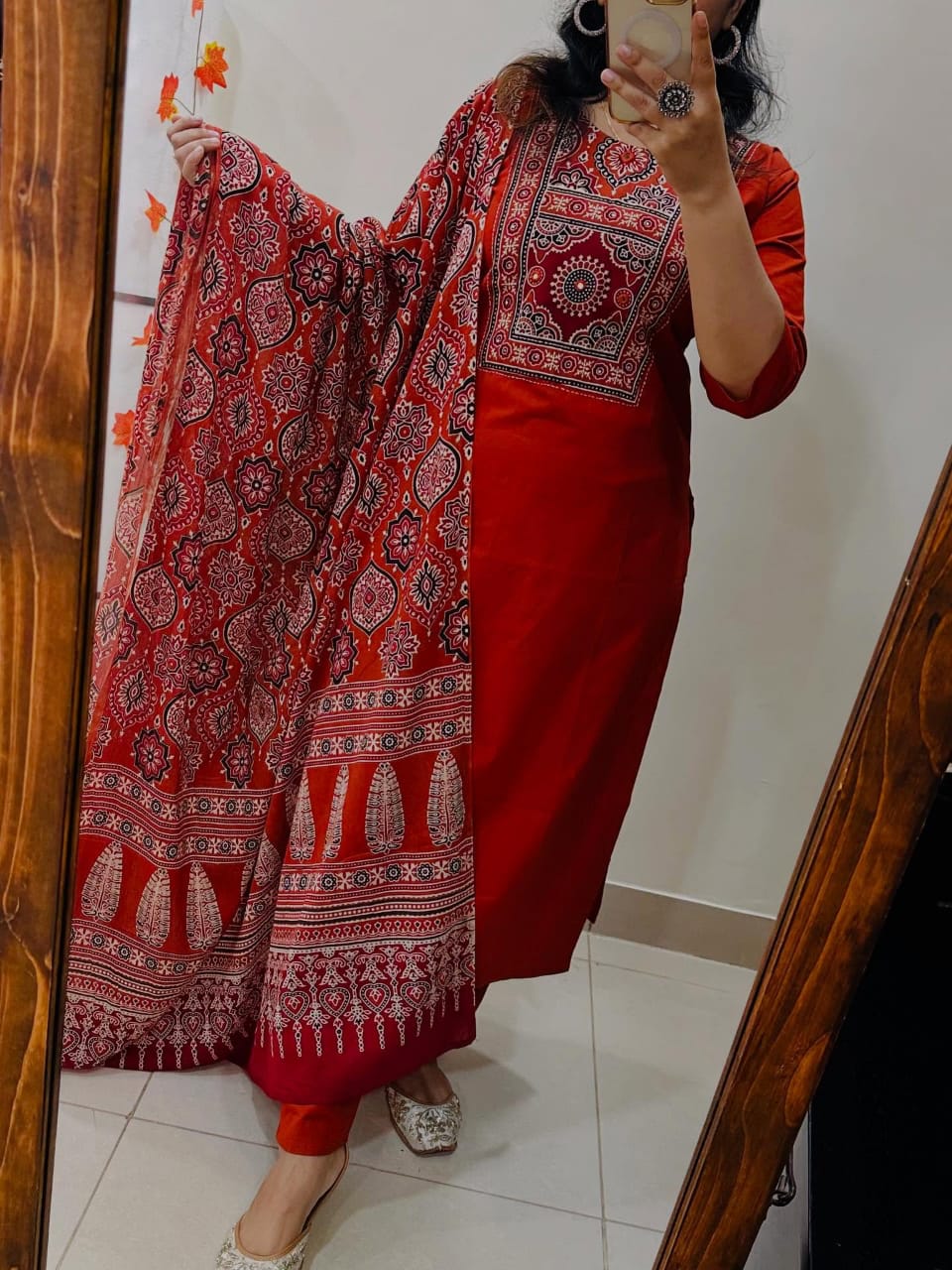 Person wearing a red traditional outfit with a patterned dupatta, taking a mirror selfie.