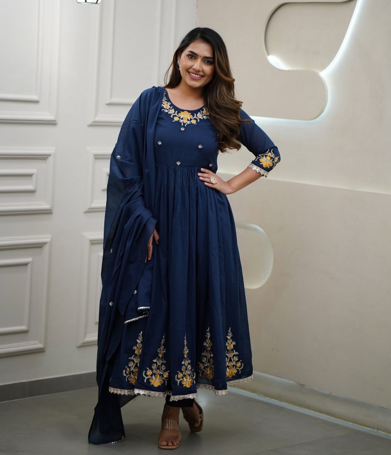 Woman wearing a navy blue traditional outfit with gold embroidery in a well-lit room.