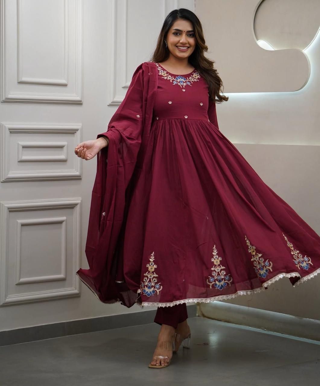 Woman wearing a maroon traditional outfit with floral embroidery in a well-lit room.