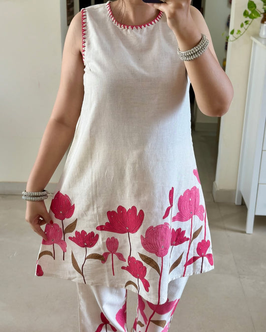White sleeveless dress with pink floral patterns worn by a person indoors.