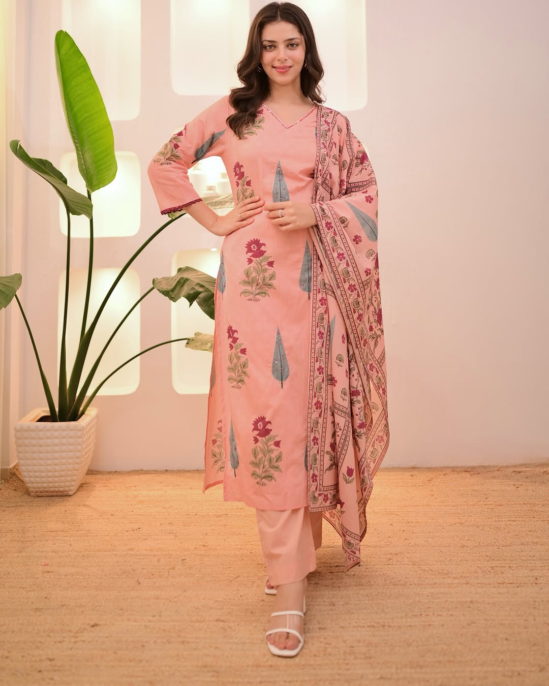 Woman wearing a pink traditional outfit with floral patterns in a well-lit room.