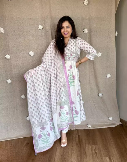 Woman in a floral dress standing against a neutral wall with decorative elements.